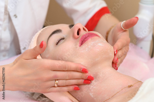 Applying cream to a woman's face with massaging movements by a beautician.