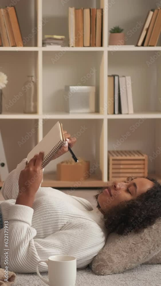 Vertical video. Creative writing. Woman author. Home leisure. Dreamy female planning in diary enjoying relaxing on room floor cozy cushion. Vertical video. Creative writing. Woman author. Home leisure. Dreamy female planning in diary enjoying relaxing on room floor cozy cushion.