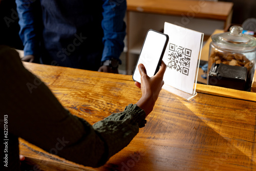 Fotografie Hand of african american woman scanning qr code using smartphone in cafe