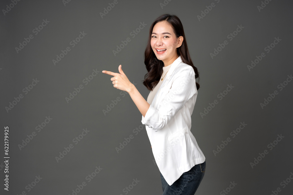 Asian female executive with long hair Turn sideways, point your finger towards the destination. Wearing a white suit and jeans, excited faces, bright smiles. Take a photo in the gray background studio Asian female executive with long hair Turn sideways, point your finger towards the destination. Wearing a white suit and jeans, excited faces, bright smiles. Take a photo in the gray background studio