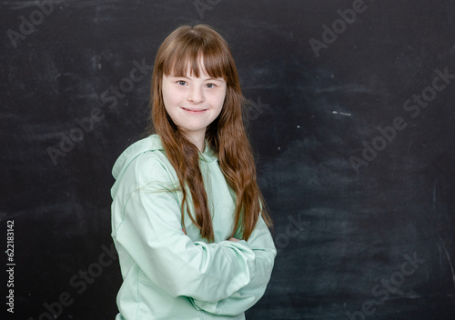 Happy young girl with Downs syndrom stands near chalkboard at the school