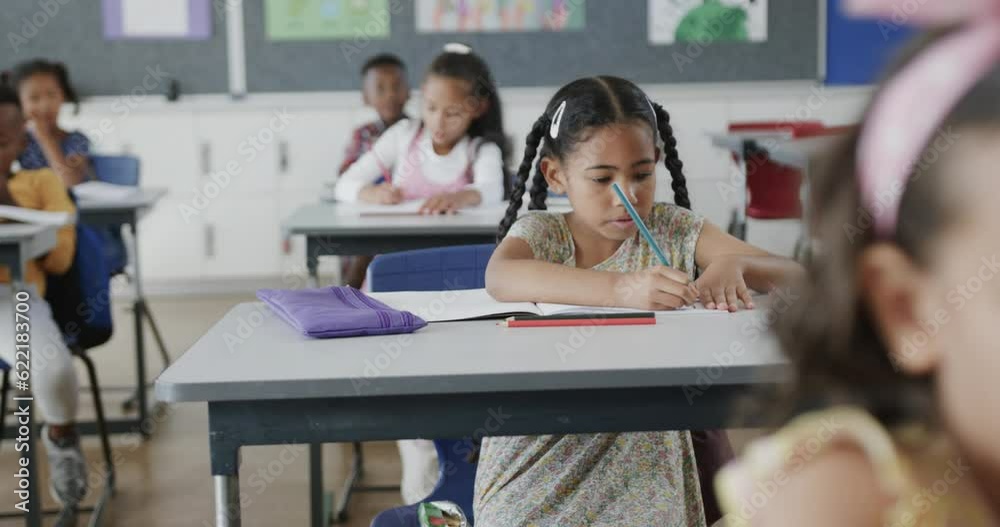 Focused diverse schoolchildren writing at desks in elementary school classroom, slow motion Focused diverse schoolchildren writing at desks in elementary school classroom, slow motion