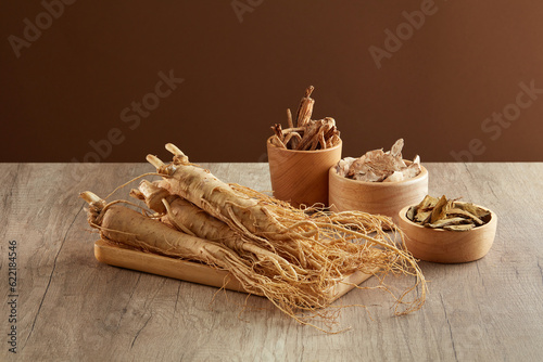 A tray of Ginseng roots displayed with bowls of Red ginseng, Bai zhu and Rhubarb root and rhizome. Traditional chinese medicine is very precious photo