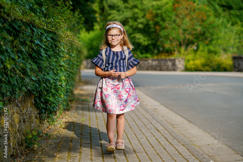 Little Preschool Girl on the Way to School. Healthy Happy Child Walking to Nursery School and Kindergarten. Smiling Child with Eyeglasses and Backpack on the City Street, Outdoors. Back to School. © Irina Schmidt