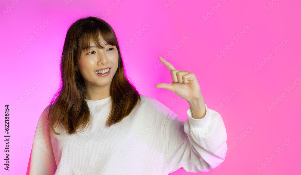 Young asian woman long hair style in white long sleeve t shirt posing smiling and pinching fingers on pink neon background. Young asian woman long hair style in white long sleeve t shirt posing smiling and pinching fingers on pink neon background.