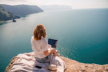 Freelance woman working on a laptop by the sea, typing away on the keyboard while enjoying the beautiful view, highlighting the idea of remote work.