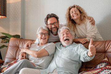 Happy bonding family group sitting on sofa at home having fun and laughing. Handsome  people, parents and adult sons, two generations looking at camera