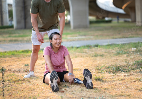 Happy exercise Asia woman with prosthetic leg and caucasian friend stretching at the park city 