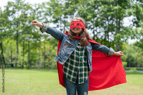 Caucasian girl having fun wearing red mask, red cape, running cross like a fly in the park. The superhero concept saves the global environment and enjoylife. photo