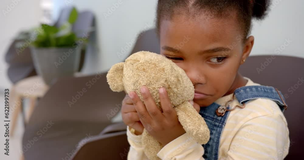 Sad african american girl sitting in hospital waiting room and holding mascot, slow motion Sad african american girl sitting in hospital waiting room and holding mascot, slow motion
