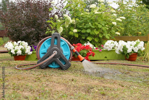 Watering flowers and plants in summer garden by the hose reel and sprayer nozzle. 