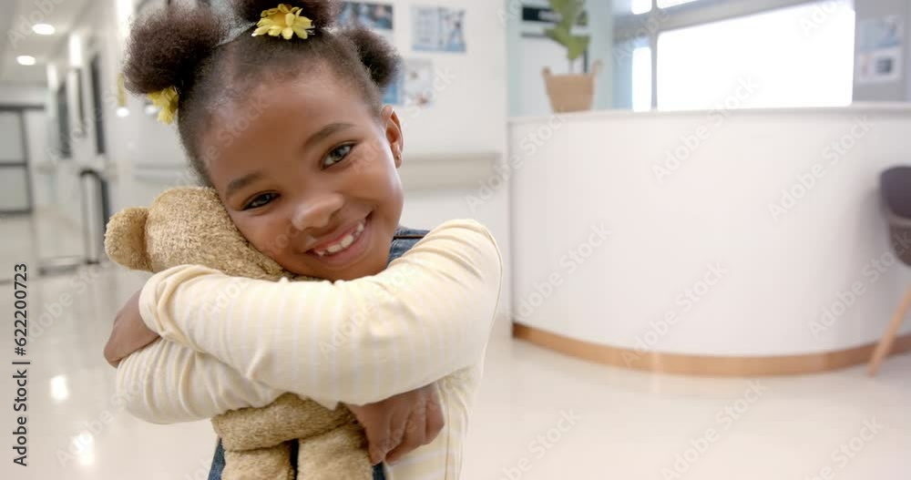 Portrait of happy african american girl hugging mascot in hospital, slow motion