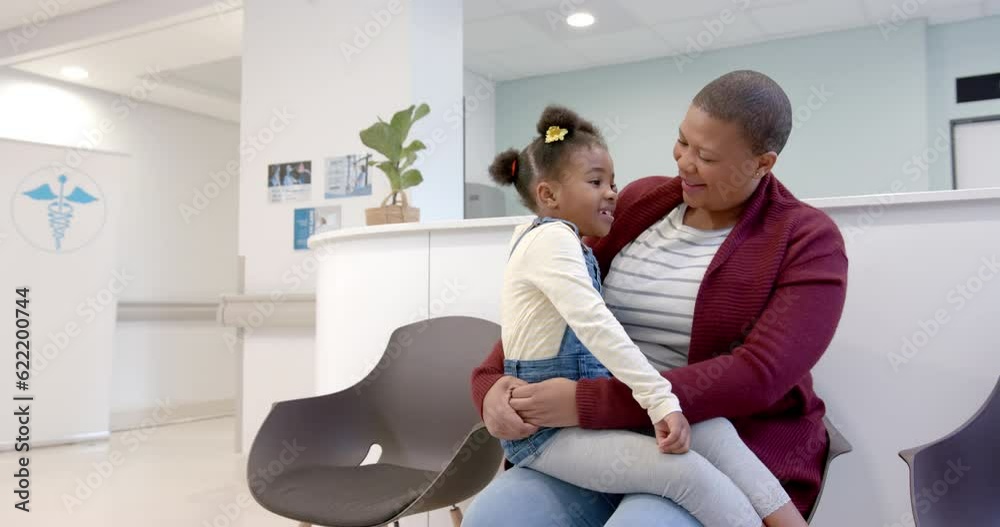Happy african american mother holding daughter on knees in hospital waiting room, slow motion
