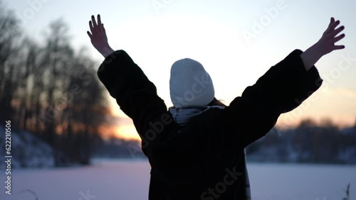 Back view unrecognizable excited woman stretching hands in slow motion admiring winter sunrise in dusk. Happy cheerful Caucasian lady enjoying weekend leisure at dawn outdoors