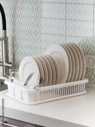 A plastic dish drying rack stands at the sink in the kitchen with clean dishes inside. photo