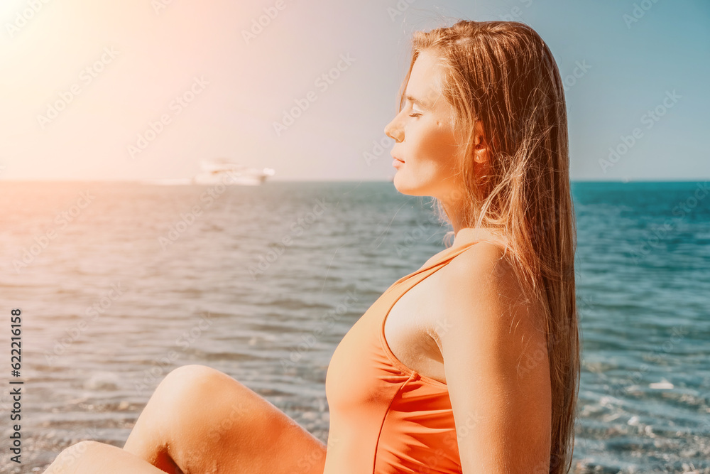 Young woman in red bikini on Beach. Girl lying on pebble beach and enjoying sun. Happy lady with long hair in bathing suit chilling and sunbathing by turquoise sea ocean on hot summer day. Close up