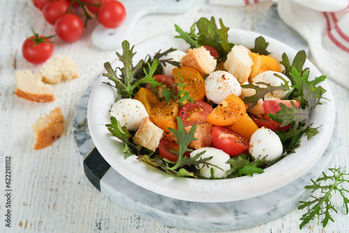 Tuscan Panzanella. Cherry Tomatoes salad with arugula, basil, mozzarella and bread crackers on white bowl. Traditional italian salad. Mediterranean healthy food and cuisine.