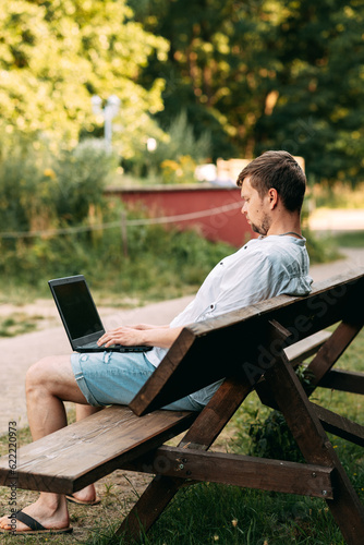 Portrait of a handsome man working with laptop sitting on a bench © Viktoriia