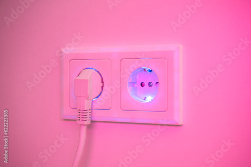 Blue and pink illuminated socket with plug inserted to symbolise power consumption and electrical energy from a socket outlet photo