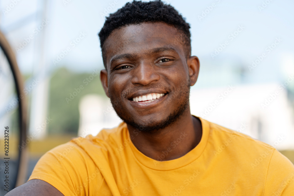Authentic portrait of handsome smiling African American man wearing yellow casual t shirt looking at camera on the street Authentic portrait of handsome smiling African American man wearing yellow casual t shirt looking at camera on the street