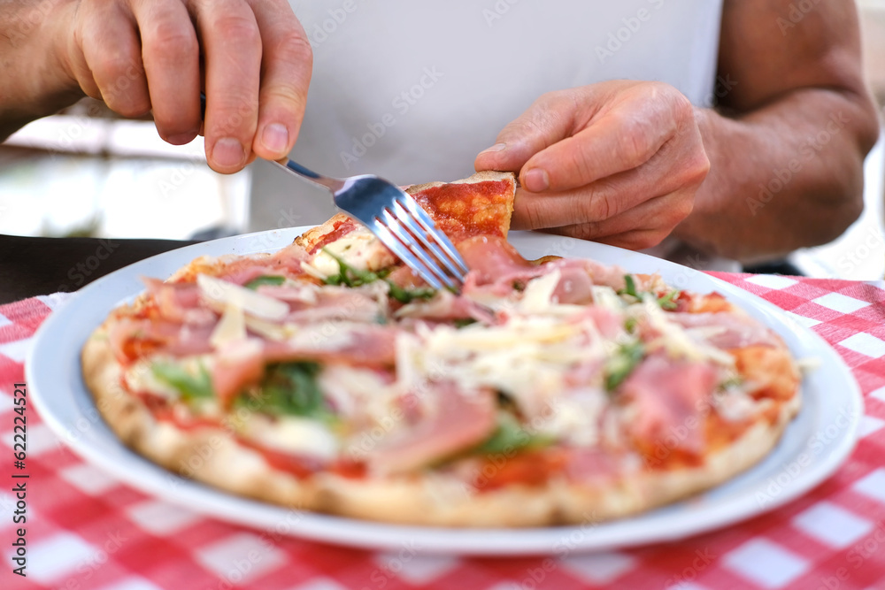plate with round italian pizza cut into slices on table, male hands take pieces of pizza with salami, cheese, arugula, hands with food close-up, concept family pleasure, culinary tradition, fast food plate with round italian pizza cut into slices on table, male hands take pieces of pizza with salami, cheese, arugula, hands with food close-up, concept family pleasure, culinary tradition, fast food