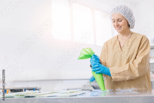 Young woman confectioner squeezes liquid chocolate from pastry bag. Process chocolate bar on candy factory photo