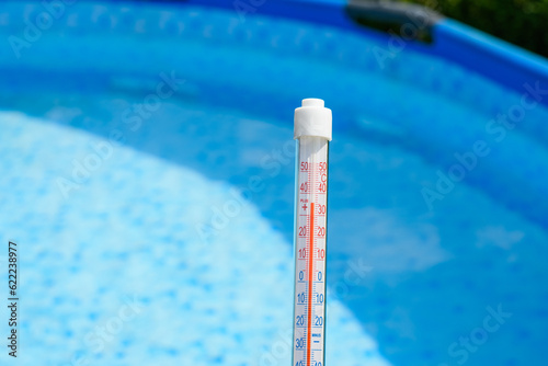 Termometr trzymany w ręce na tle basenu ogrodowego mierzy temperaturę w słońcu 