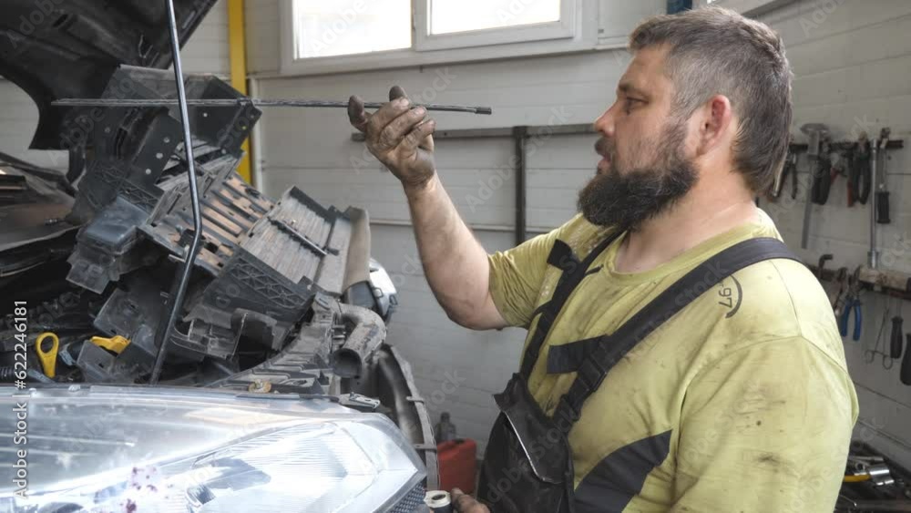 Professional bearded repairman fixing car with open hood at workshop. Auto mechanic in uniform working with vehicle at garage. Concept of automobile maintenance and diagnostic. Slow motion Close up Professional bearded repairman fixing car with open hood at workshop. Auto mechanic in uniform working with vehicle at garage. Concept of automobile maintenance and diagnostic. Slow motion Close up