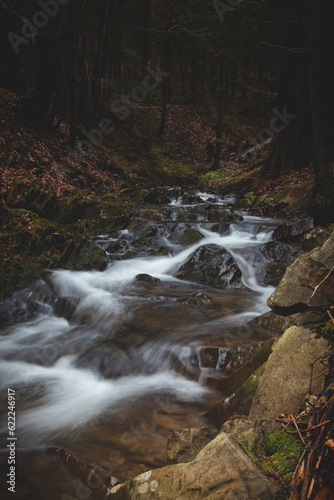 Stream of water rushes through a rocky riverbed in the Beskid forests in autumn weather. Long exposure  flowing water