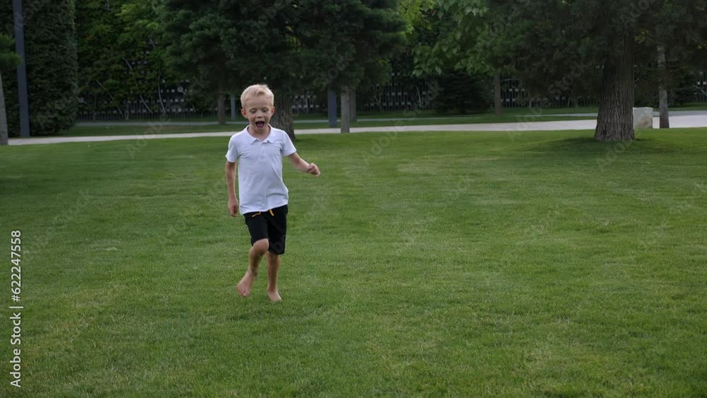 Funny girl and boy running barefoot on the lawn in the park in the evening at sunset, children running and laughing. The boy runs across the grass and falls. Children's fun in the city park in summer. Funny girl and boy running barefoot on the lawn in the park in the evening at sunset, children running and laughing. The boy runs across the grass and falls. Children's fun in the city park in summer.