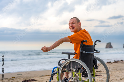 A disabled person on his back in a wheelchair on the beach in summer by the sea