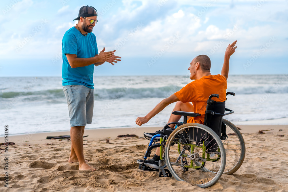 A disabled person in a wheelchair on the beach with a friend having fun dancing