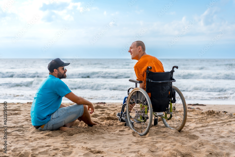 Fototapeta premium Portrait a disabled person in a wheelchair on the beach with a friends sitting looking at the sea