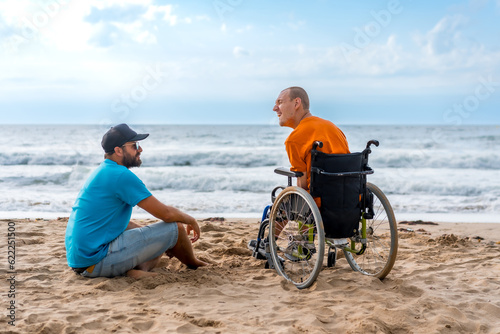 Portrait a disabled person in a wheelchair on the beach with a friends sitting looking at the sea