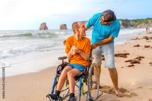 A disabled person in a wheelchair on the beach pushed by a friends by the sea, enjoying the summer