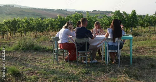 Happy adult people enjoy pic nic at wineyard - Multiracial friends eating outdoor and tasting red wine during summer time  photo