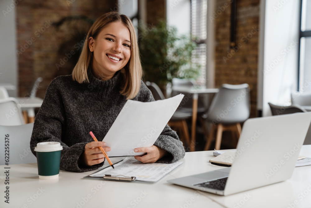 Young smiling woman doing paperwork while sitting in office Young smiling woman doing paperwork while sitting in office