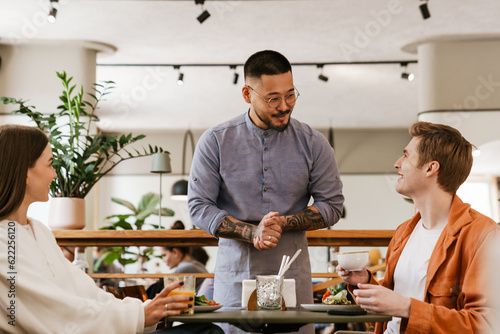 Photography Smiling waiter serving couple in cafe