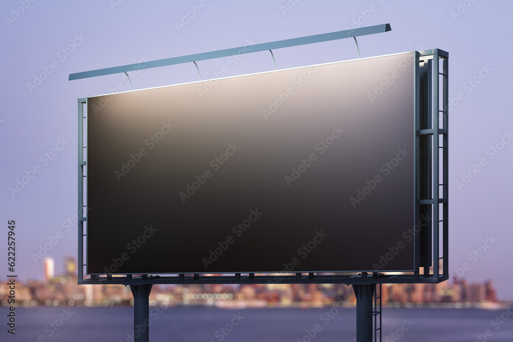 Blank black billboard on city buildings background at night, perspective view. Mockup, advertising concept