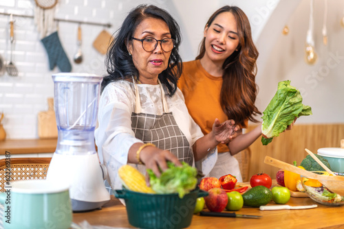 Portrait of happy love asian family senior mature mother and young daughter smiling cooking vegan food healthy eat with fresh vegetable salad and fruit in kitchen, care, insurance, elderly health care