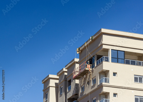 Building in construction and external elevator for painters in a day with a blue sky in the background. © Stefano