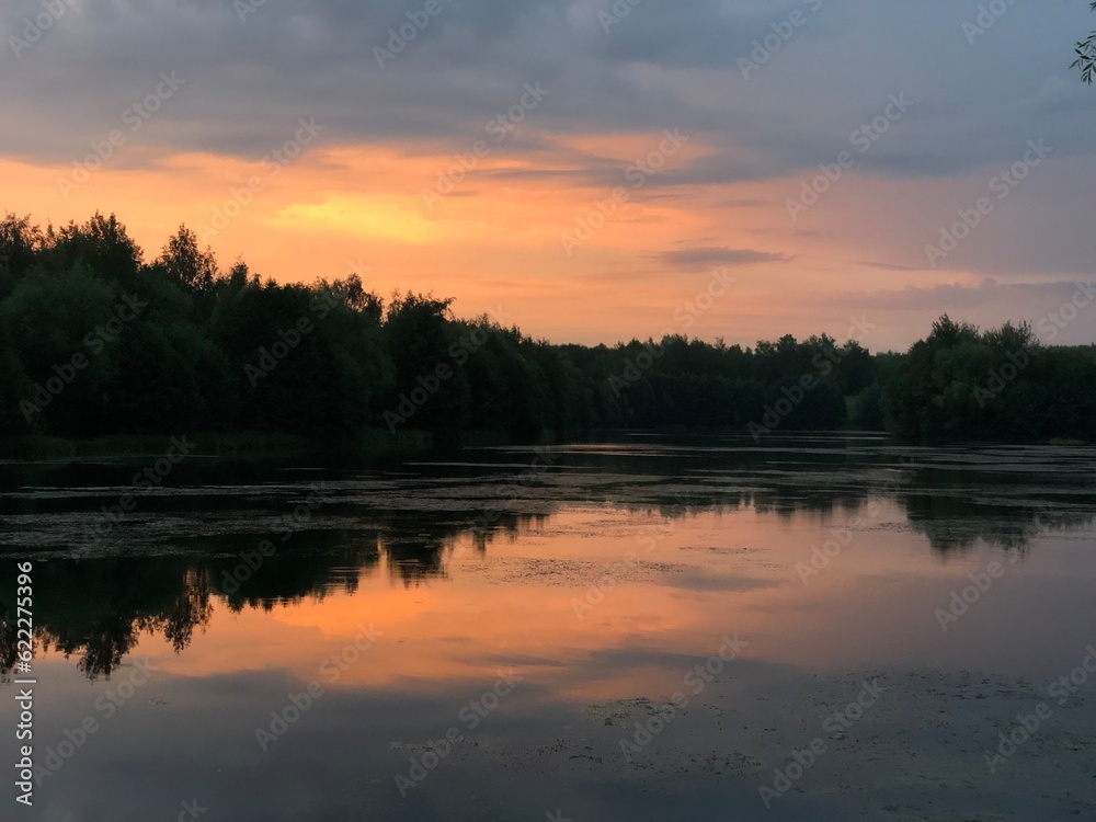 warm sunset over calm lake with cloudy sky and forest silhouetted on horizon summer nature background