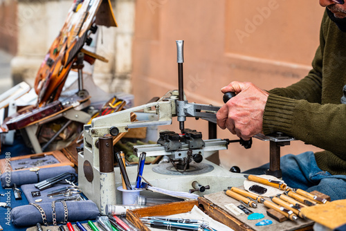 Elderly engraver at work on a street bench. Detail of the hands engrave plaques, pens and other objects. Old jobs. photo