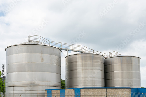 Three large silver metal tanks against a cloudy sky. A metal staircase with railings passes from above.