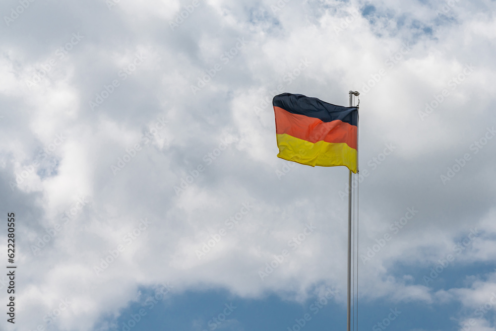 German national flag on a metal mast flutters in the wind against a cloudy sky. German national flag on a metal mast flutters in the wind against a cloudy sky.