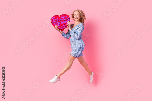 Full length profile portrait of cheerful carefree person jumping hands hold large heart symbol collage isolated on pink color background