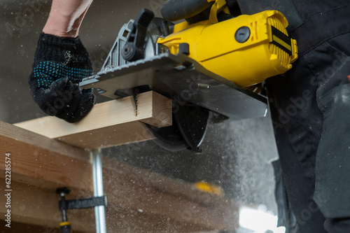 Master cuts the board with a circular saw in the workshop. Close-up of a carpenter's hands at work.  © Михаил Решетников