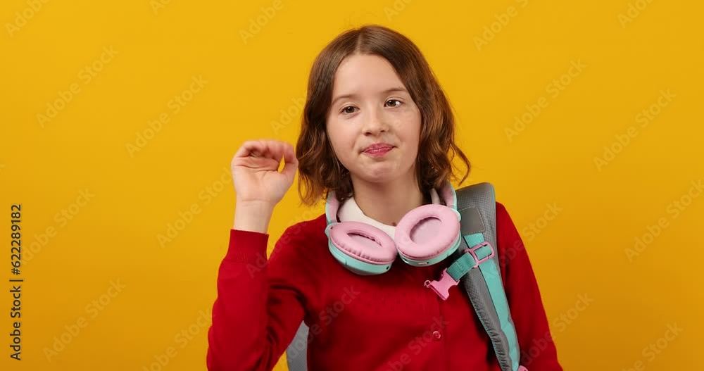 Stylish school teenage girl in headphone with a backpack on her shoulder, waves Stylish school teenage girl in headphone with a backpack on her shoulder, waves