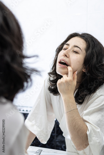 Young woman with open mouth checking teeth in mirror in home bathroom room. Brunette woman looking mouth teeth in front bathroom mirror. Teeth care, beauty and health concept