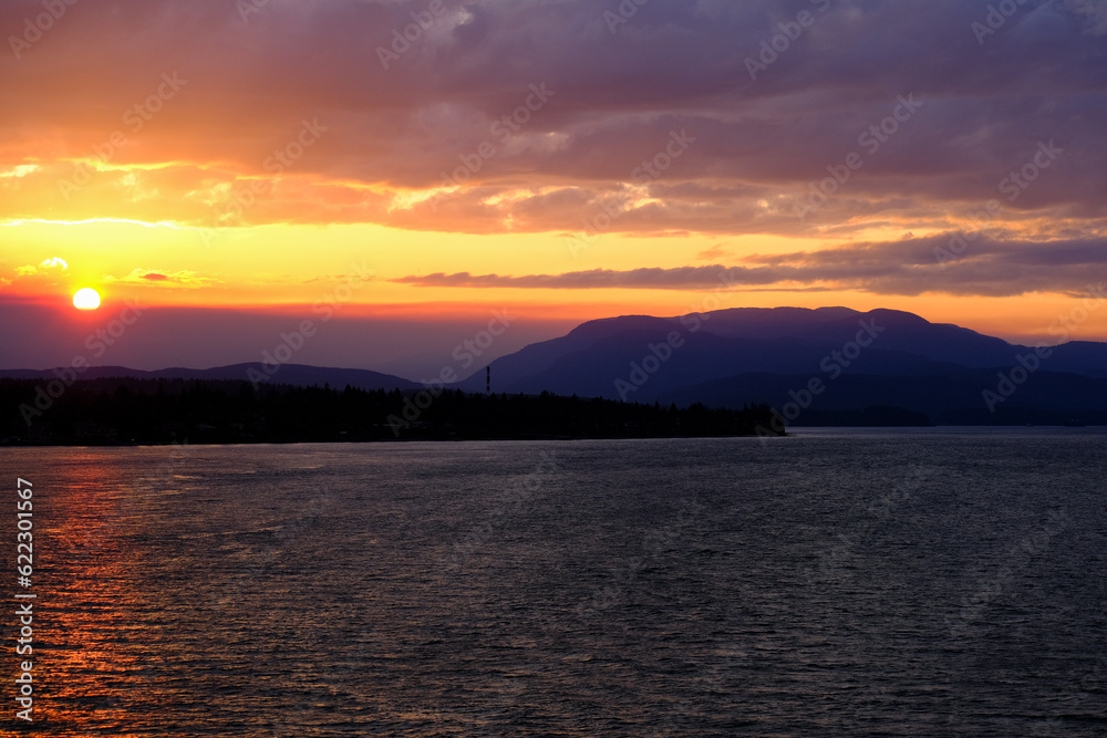 Fototapeta premium Sunset with pink, orange and purple sky above Inside Passage in British Columbia, Canada seen from cruiseship cruise ship liner returning from Alaska with mountains, shore and coast line